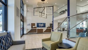 Eine moderne Lobby mit einer Rezeption, einer Sitzecke und einer Treppe zu einer oberen Ebene.