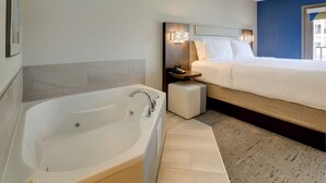 Ein modernes Hotelzimmer mit einer großen Badewanne, einem ordentlich bezogenen Bett und einem Nachttisch mit einer Lampe.
