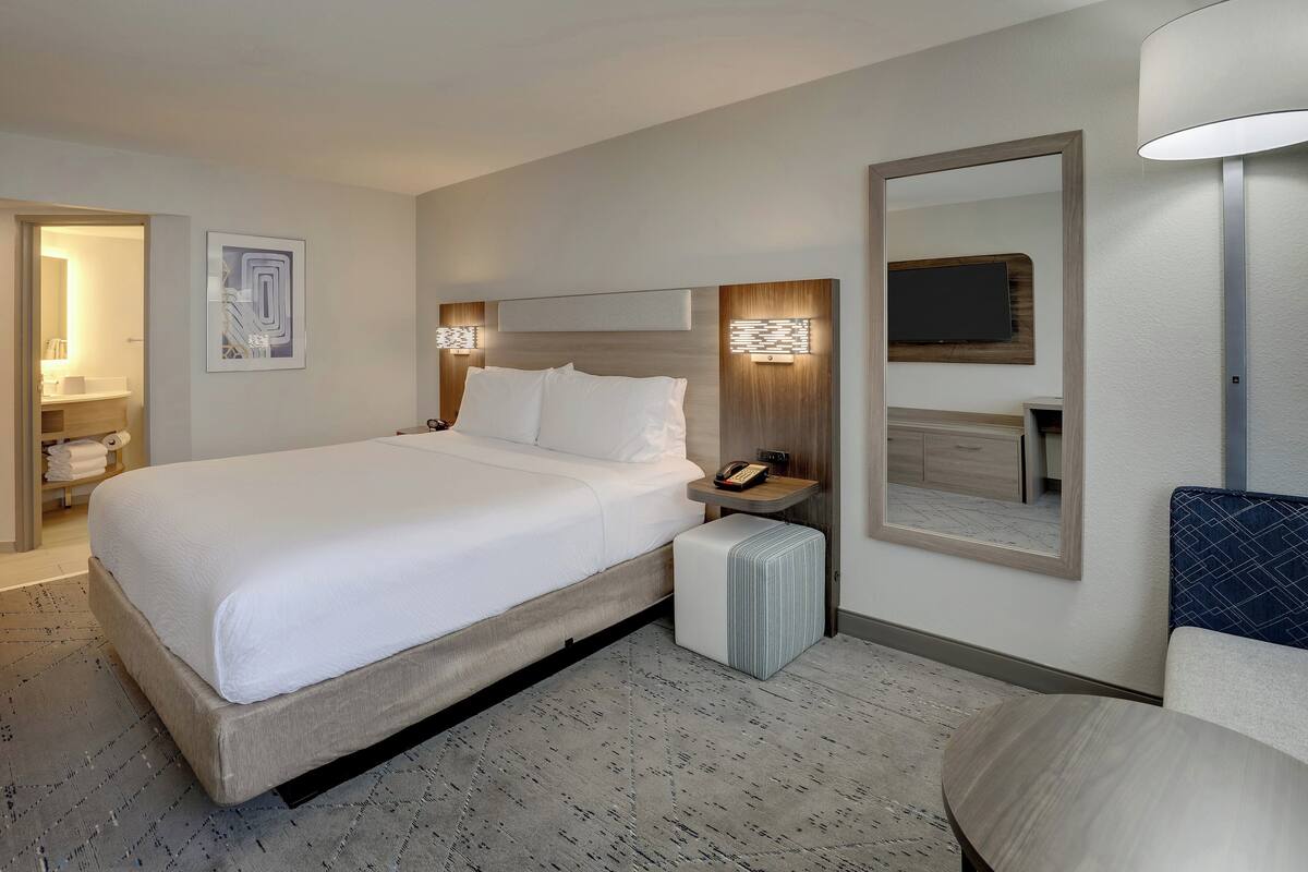 A modern hotel room with a large bed, bedside table, and a mirror.