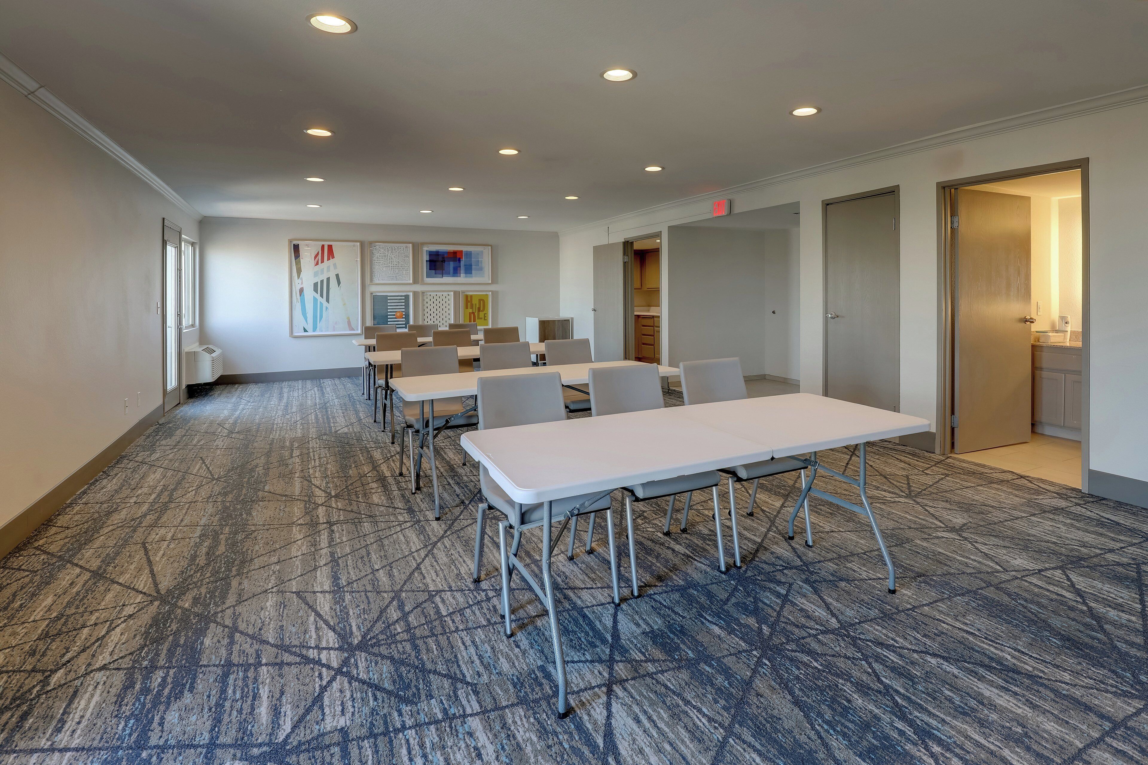 A conference room with a carpeted floor, white tables, and chairs.