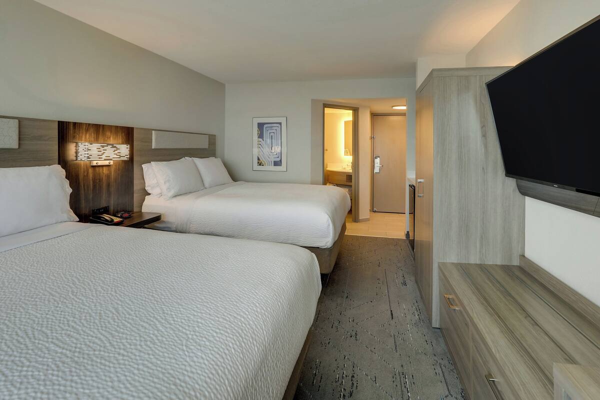 A hotel room with two beds, a flat-screen TV, a wooden headboard, and a modern light fixture.