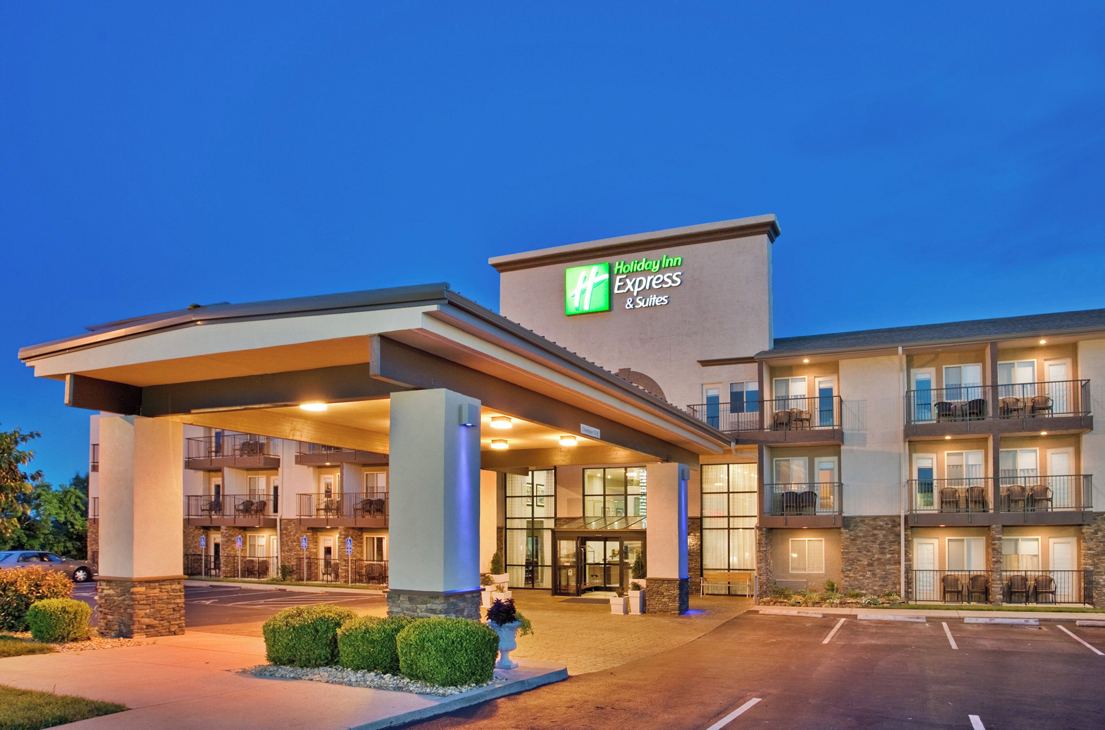 En byggnad som inrymmer ett Holiday Inn Express & Suites-hotell, med en ingång som är skyddad från väder och vind, flera balkonger och en parkeringsplats.