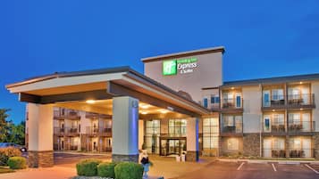 En byggnad som inrymmer ett Holiday Inn Express & Suites-hotell, med en ingång som är skyddad från väder och vind, flera balkonger och en parkeringsplats.