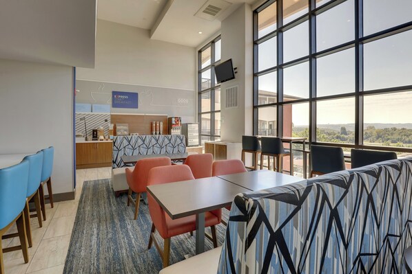 Espaço de refeições moderno em hotel, com balcão de café da manhã, assentos e amplas janelas com vista.