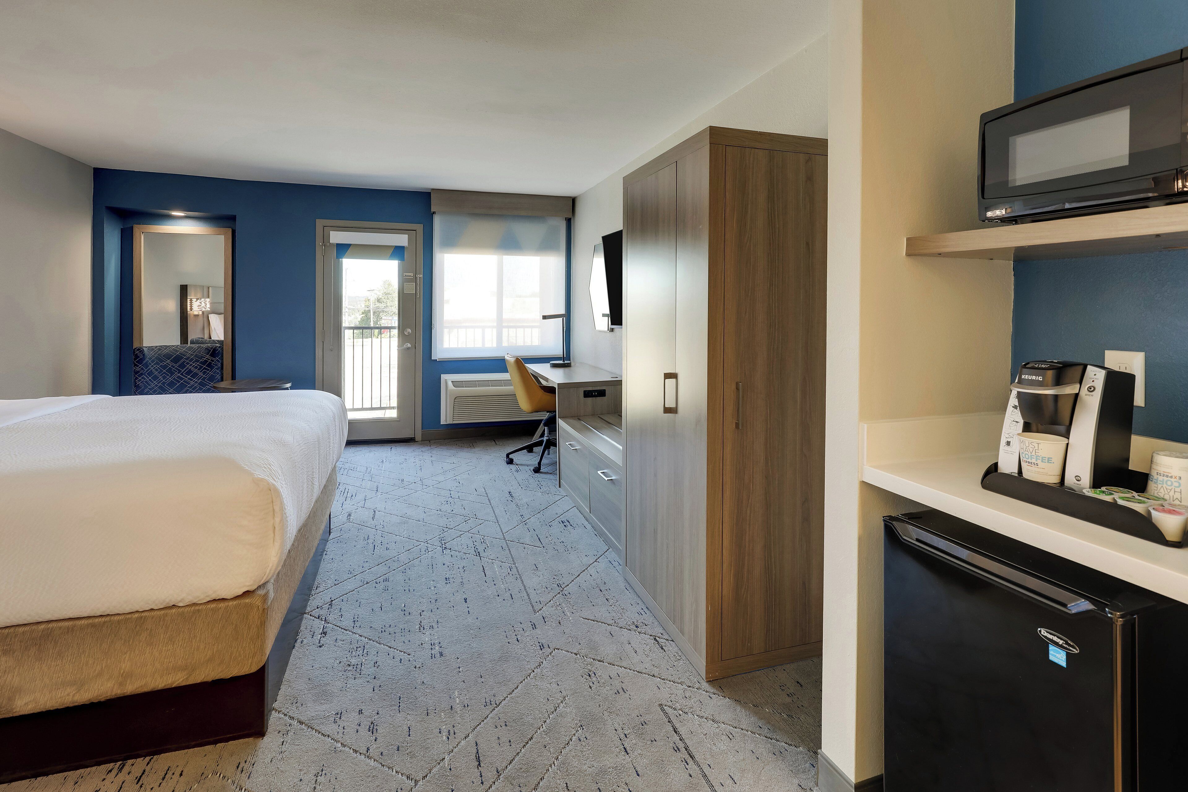 Een hotelkamer met een bed, bureau, stoel, kledingkast en een minibar.
