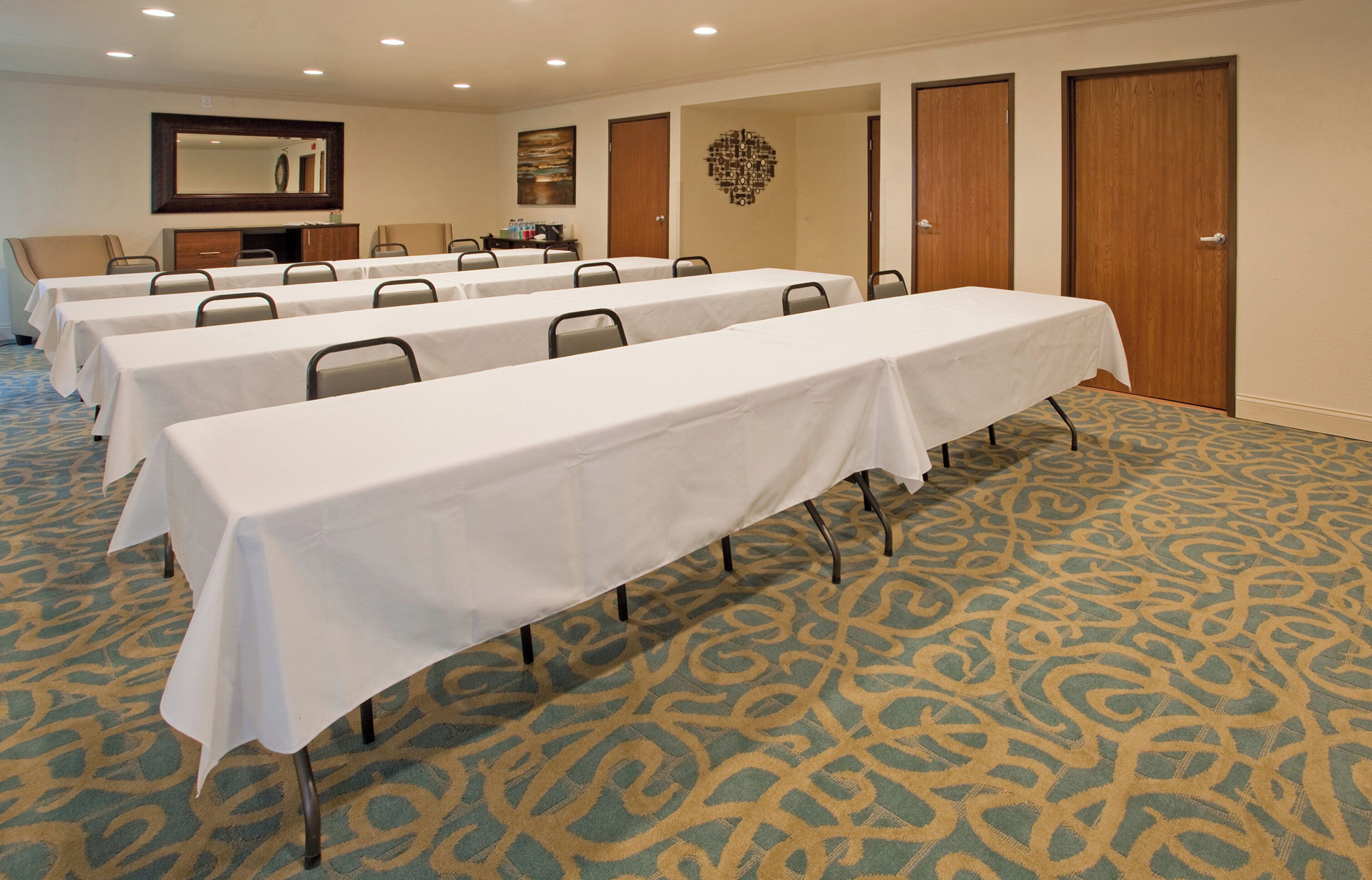 A conference room with multiple tables and chairs, carpeted floor, and doors.