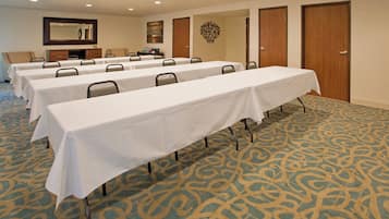 Un salón de conferencias con varias mesas y sillas, suelo alfombrado y puertas.