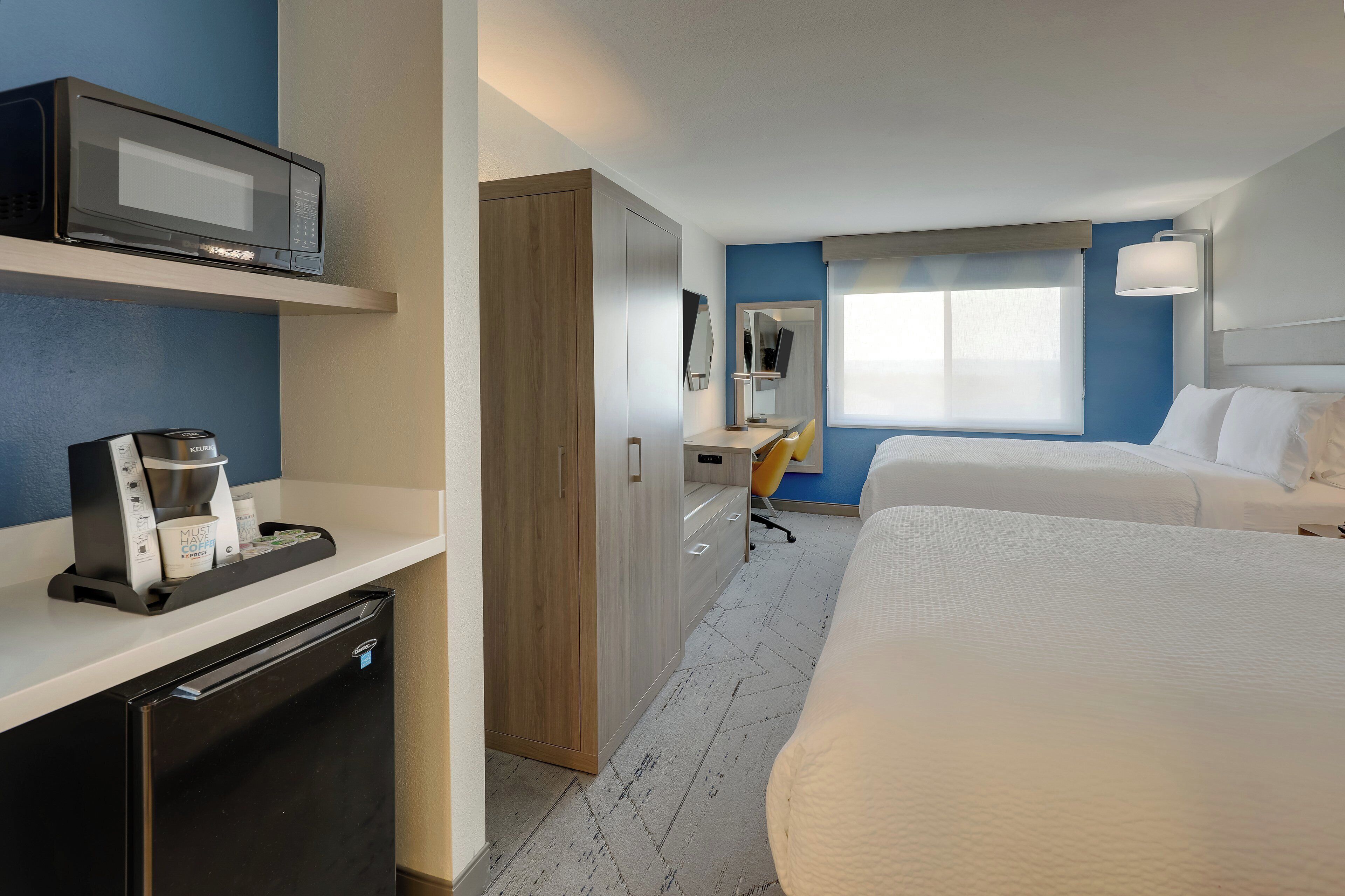 A hotel room with a bed, a desk with a chair, a microwave, a coffee maker, and a wardrobe.