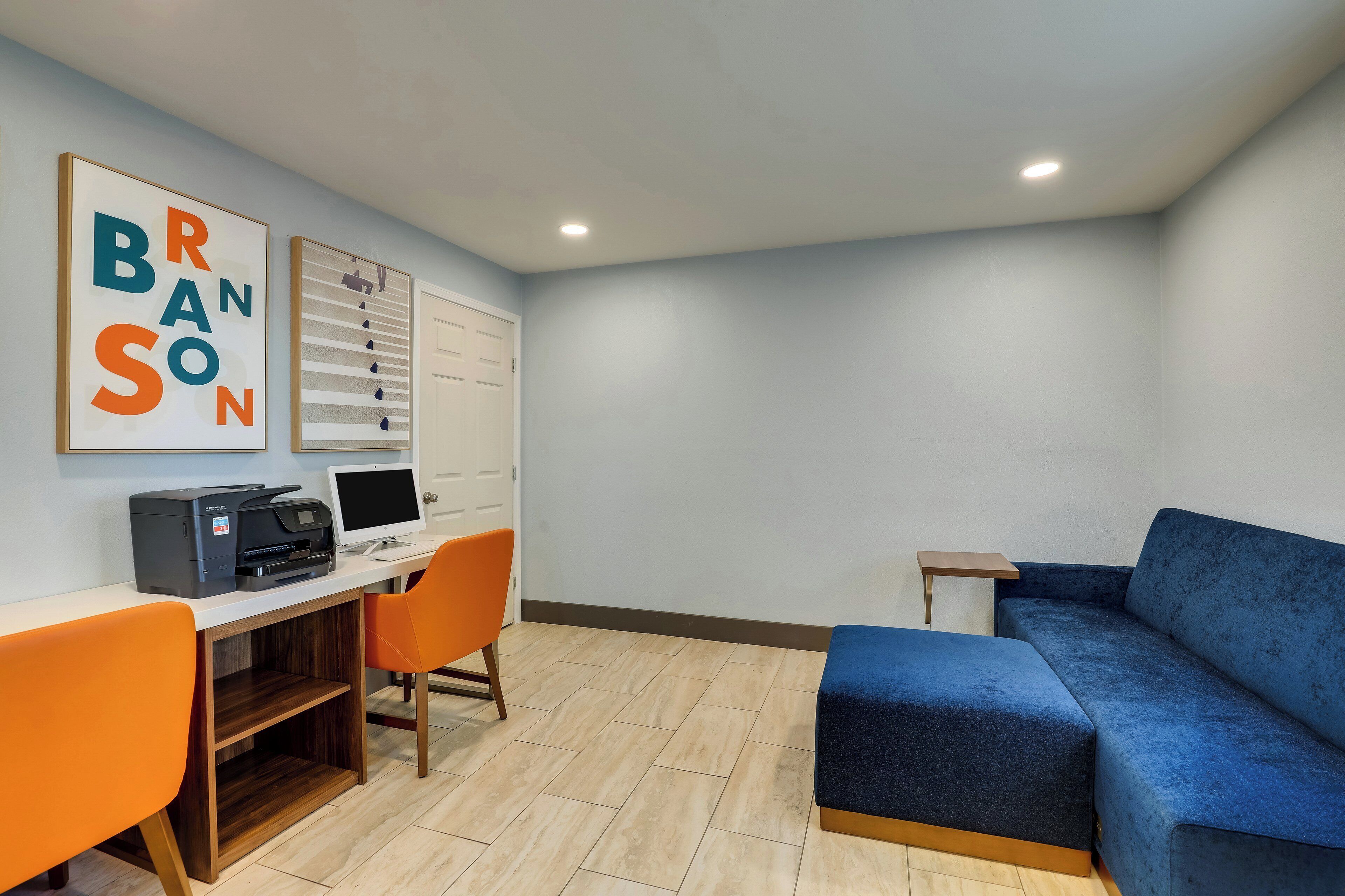 A room with a desk, two chairs, a blue sofa, a printer, and a monitor.