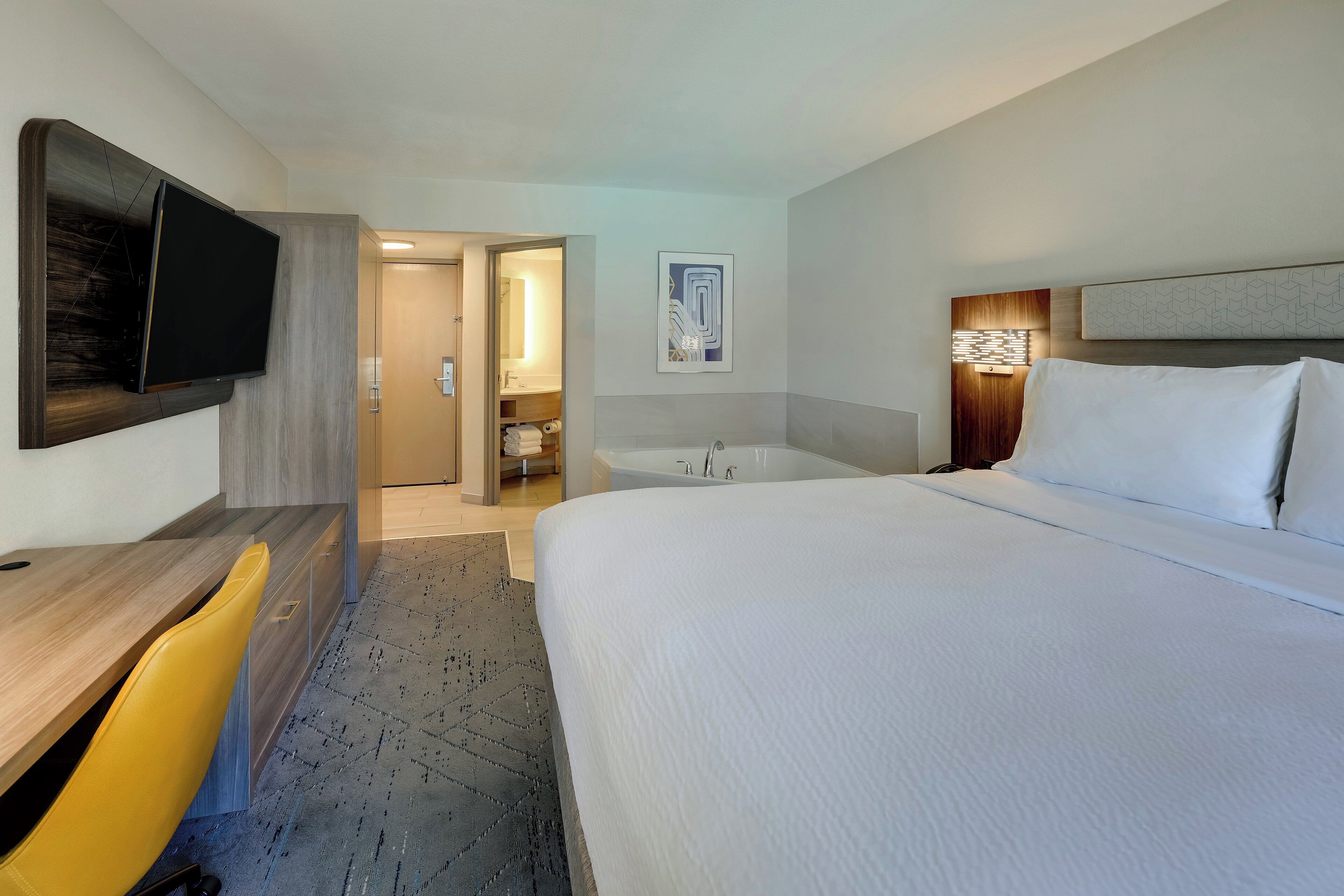 A hotel room with a bed, a desk, a chair, a TV, a bathroom with a bathtub, and a shower.