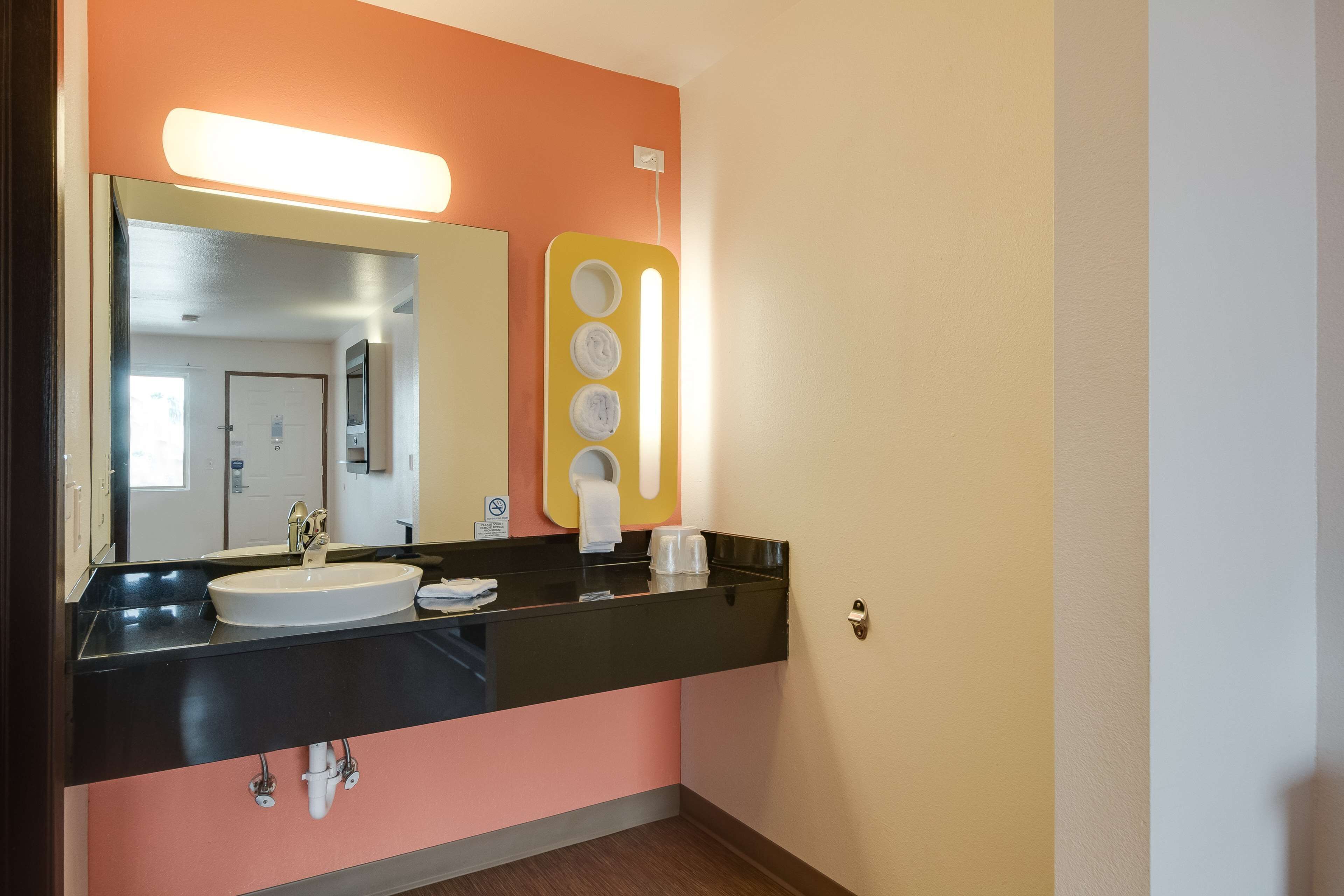 Un baño con un lavamanos negro, un espejo y un dispensador de jabón amarillo.