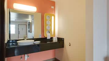 Un baño con un lavamanos negro, un espejo y un dispensador de jabón amarillo.