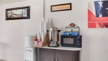 A kitchenette with a water dispenser, coffee maker, microwave, and stacked cups.