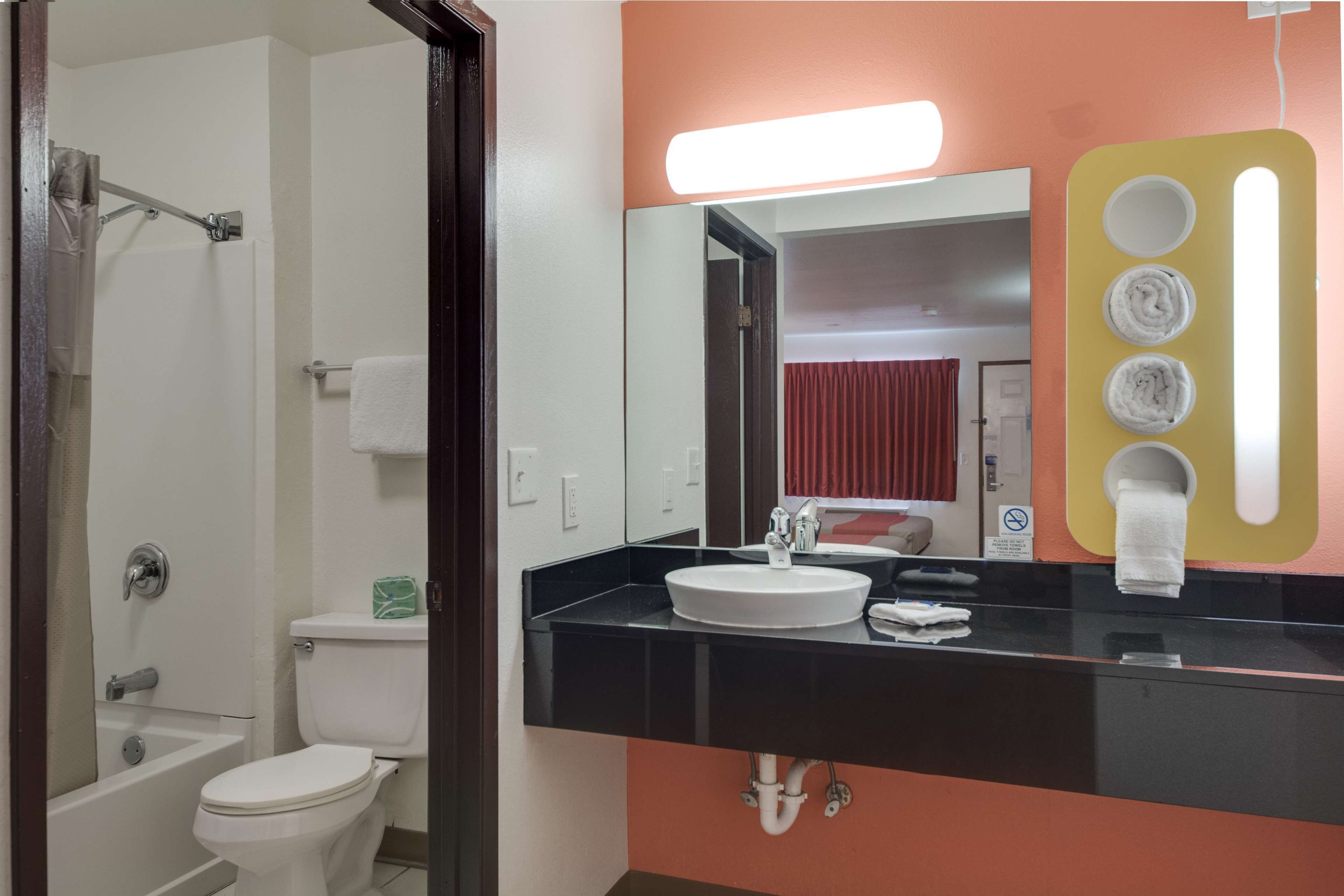 A bathroom with a white toilet, a black sink, and a mirror with a towel dispenser.