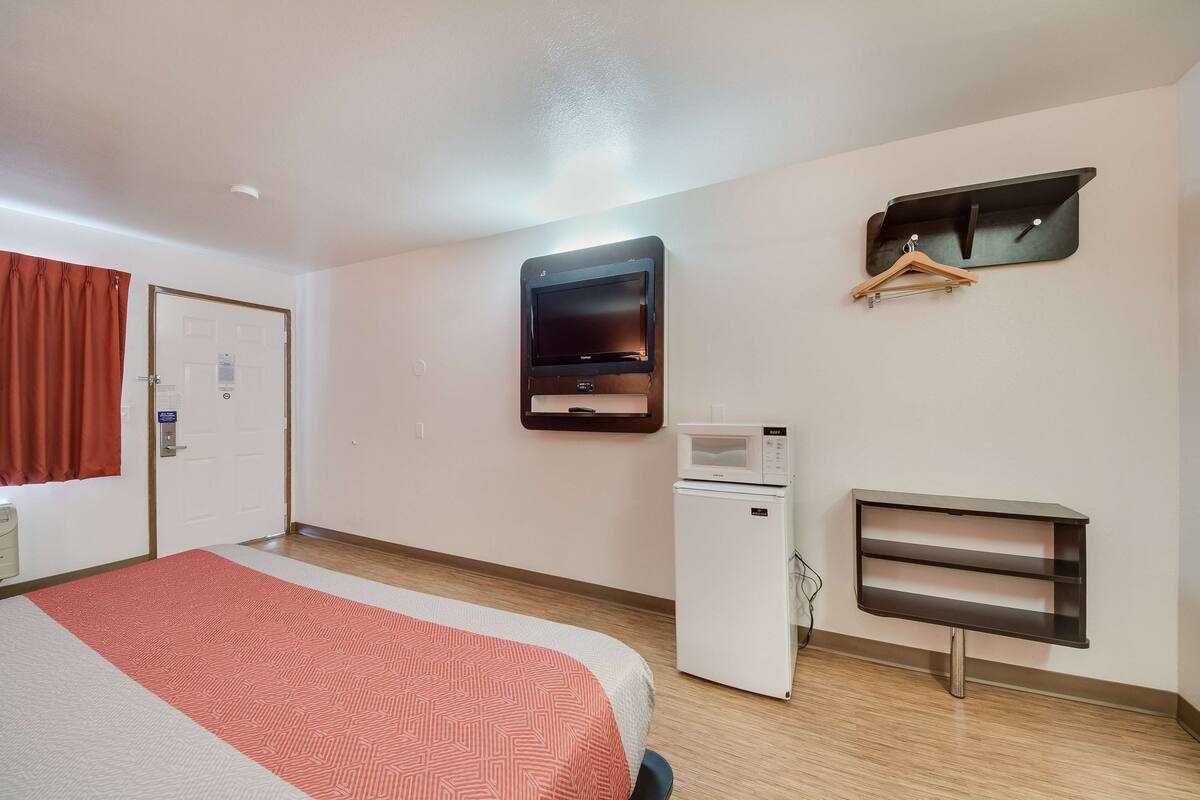 Une chambre d’hôtel équipée d’un lit, d’un four à micro-ondes, d’un petit réfrigérateur, d’un porte-manteau et d’un téléviseur fixé au mur.