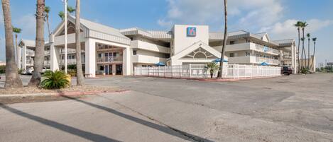 Un hotel con un letrero con el número '6', varios balcones y palmeras.