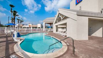 A swimming pool with a white fence, lounge chairs, and a building with a '6' sign.