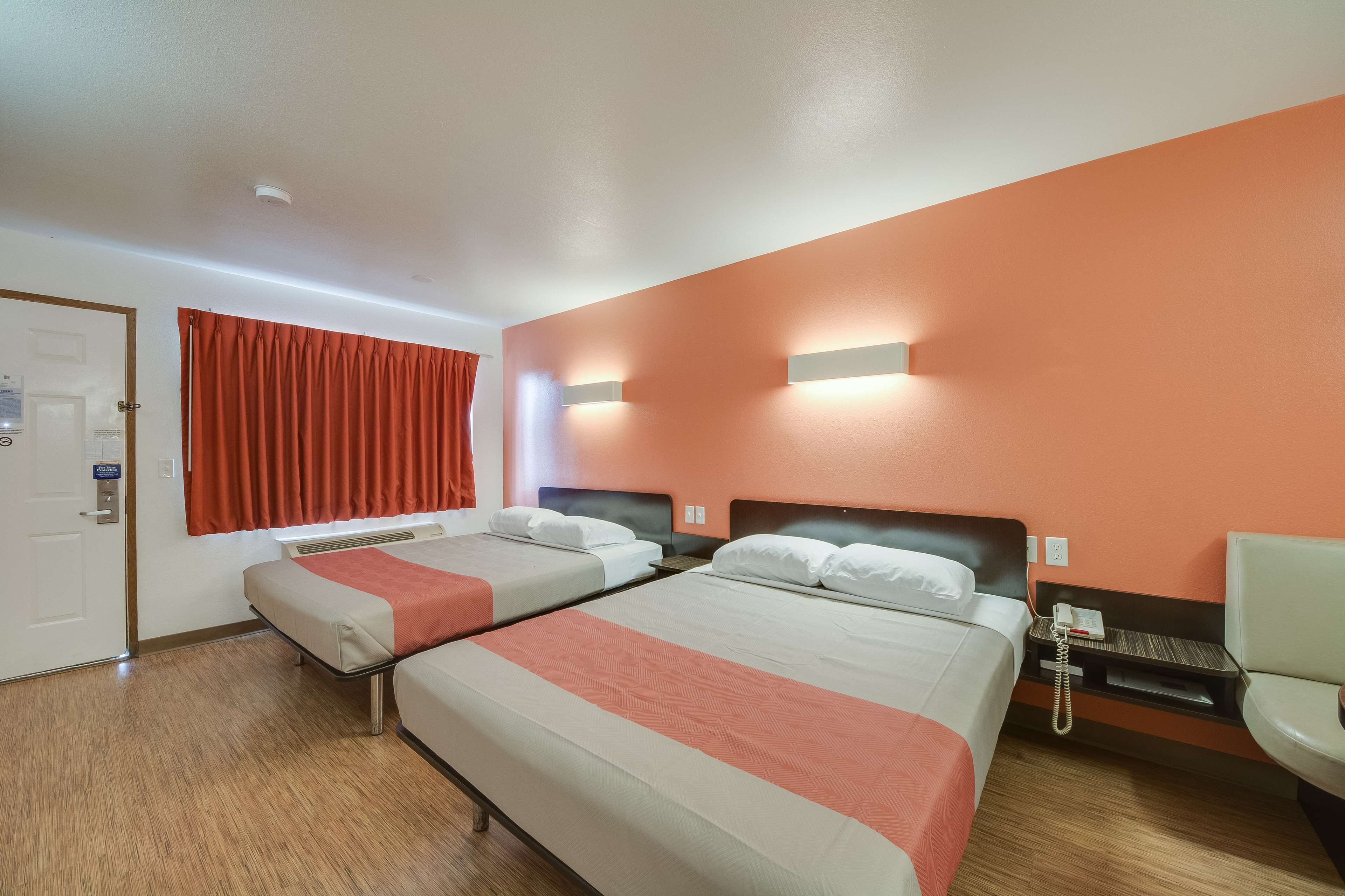 A hotel room with two beds, a desk, a chair, and a telephone.