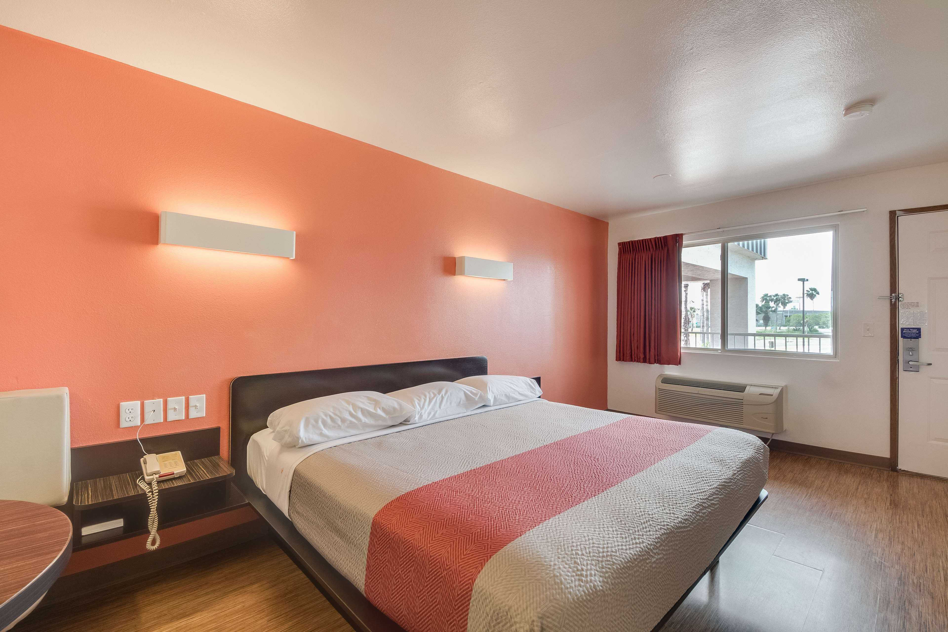 Una habitación de hotel con cama, mesita de noche y ventana con cortinas.
