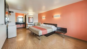 A hotel room with a bed, a desk, a chair, a refrigerator, and a bathroom visible through an open door.