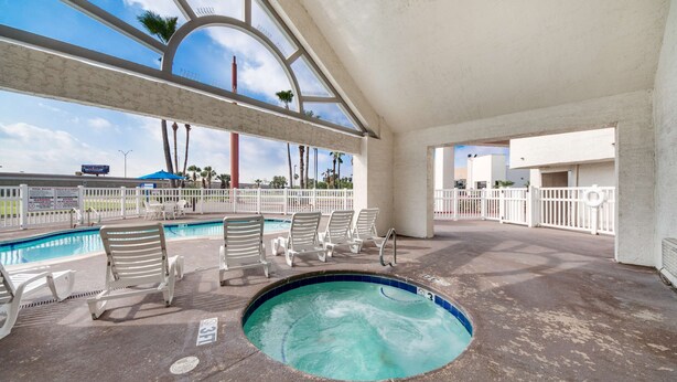 An indoor swimming pool area with lounge chairs and a hot tub.