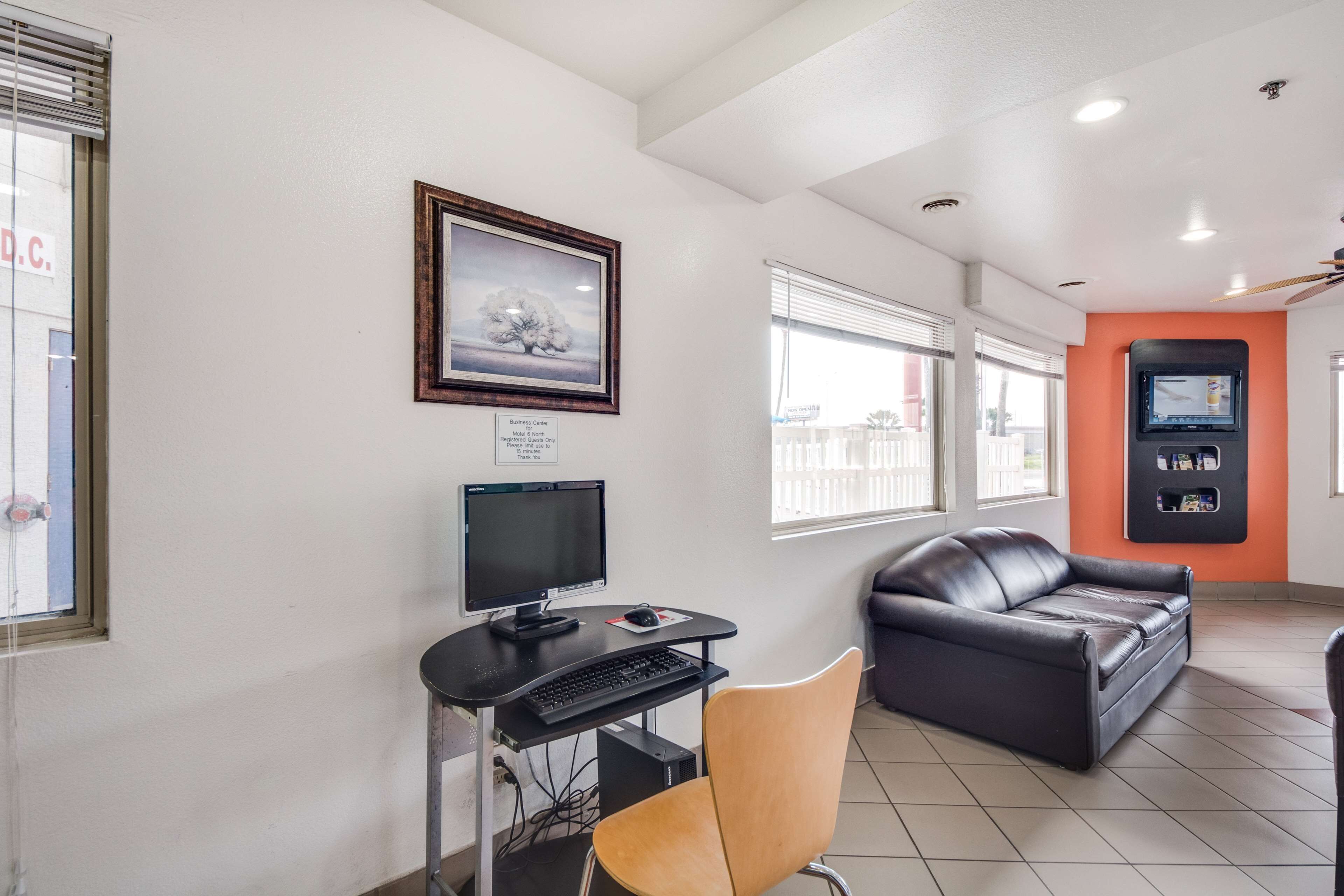 Un espacio de oficina moderno con escritorio, computadora y sillón de cuero. Hay un cuadro en la pared y un televisor sobre la pared naranja.