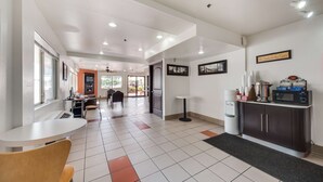 A hotel lobby with a reception desk, seating area, and a kitchenette.