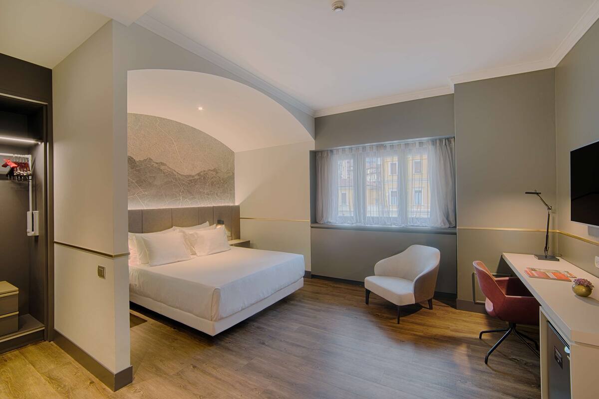 A modern hotel room with a bed, a desk, a chair, and a TV.