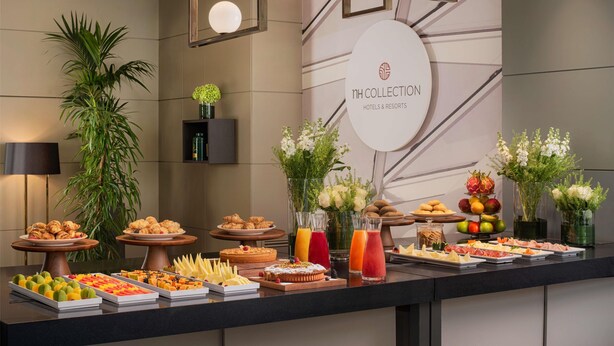 A buffet with various food items and drinks, a potted plant, and a sign for NH Collection Hotels & Resorts. - NH Collection Milano Porta Nuova (Milan)