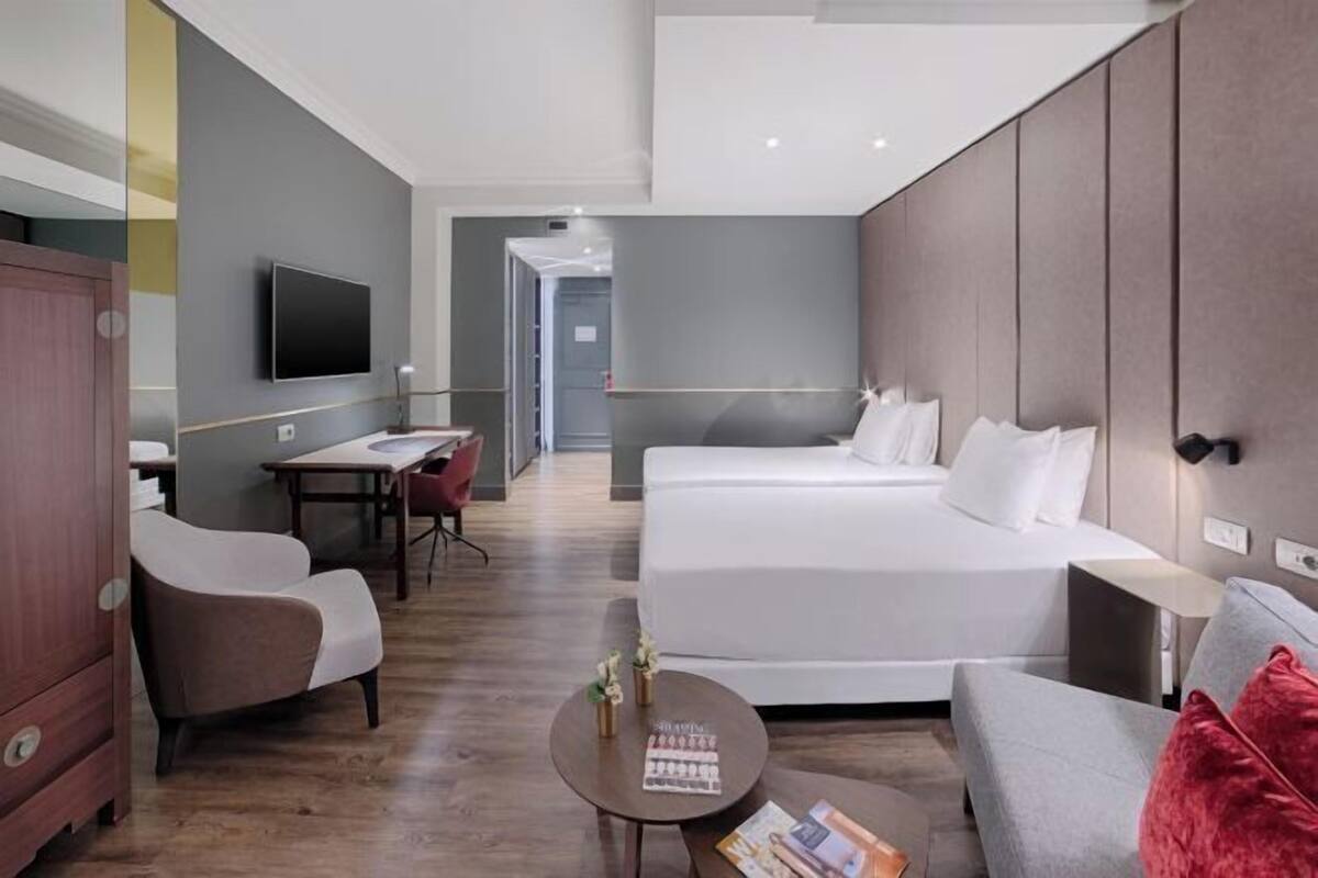 A hotel room with a large bed, a desk, a chair, a TV, and a small table with magazines.
