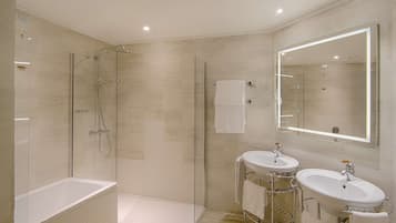 A modern bathroom with a glass-enclosed shower, a bathtub, and two sinks with a large mirror above.