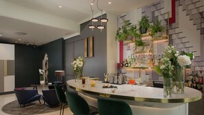 A modern kitchen with a bar area, featuring a curved island with bar stools, a countertop with various bottles, and decorative plants. - NH Collection Milano Porta Nuova (Milan)