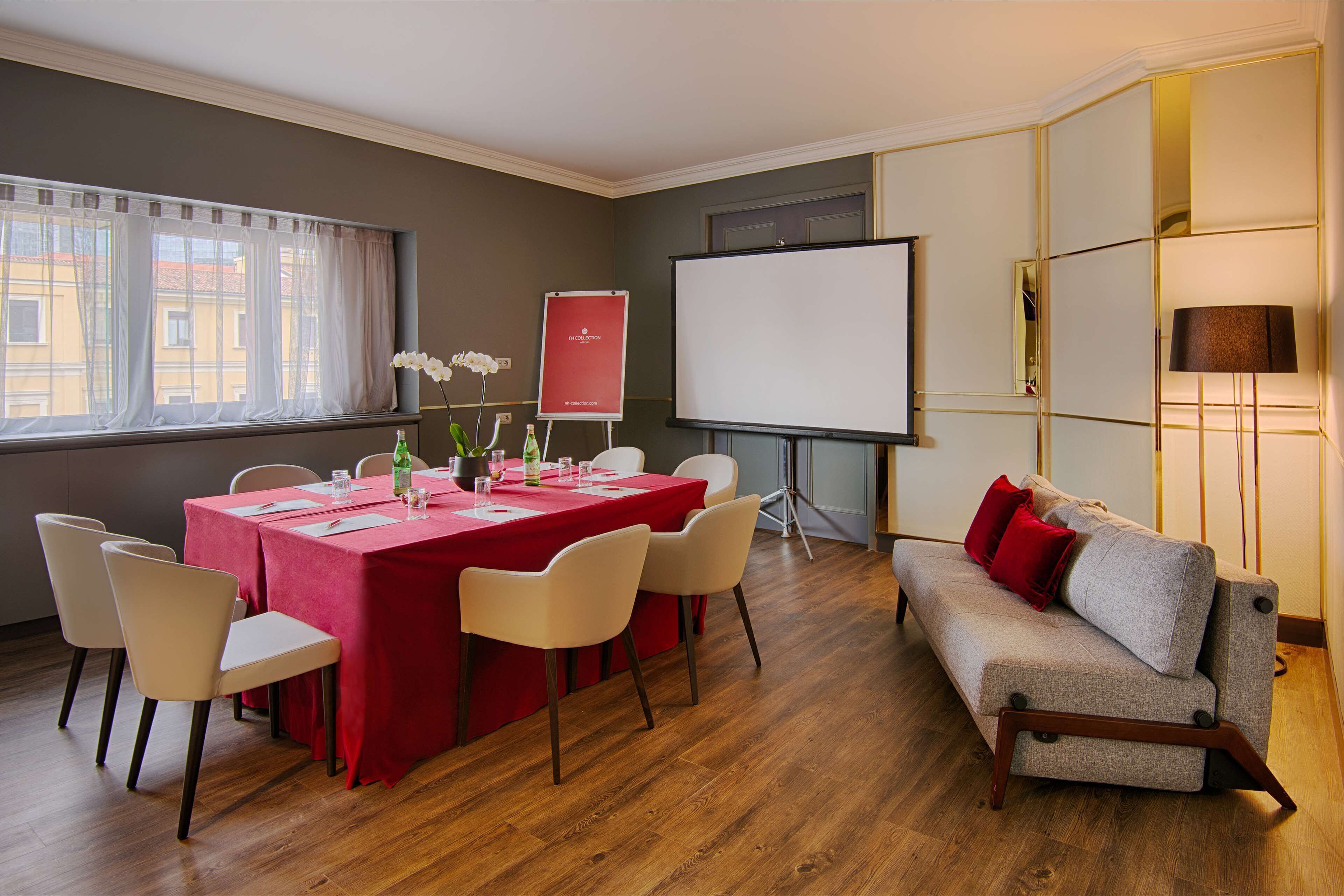 A conference room with a red table, white chairs, a whiteboard, and a sofa with red cushions.