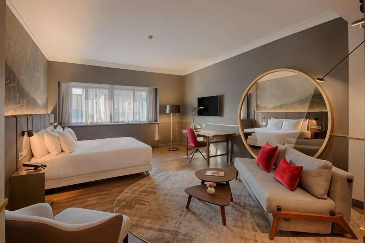 A modern hotel room with a bed, a sofa, a desk, and a large mirror.