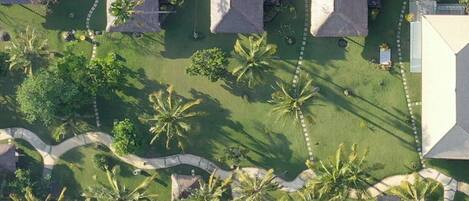 Luchtbeeld van een resort met rieten huisjes, geordend in een raster, omgeven door palmbomen en een helderblauw water.