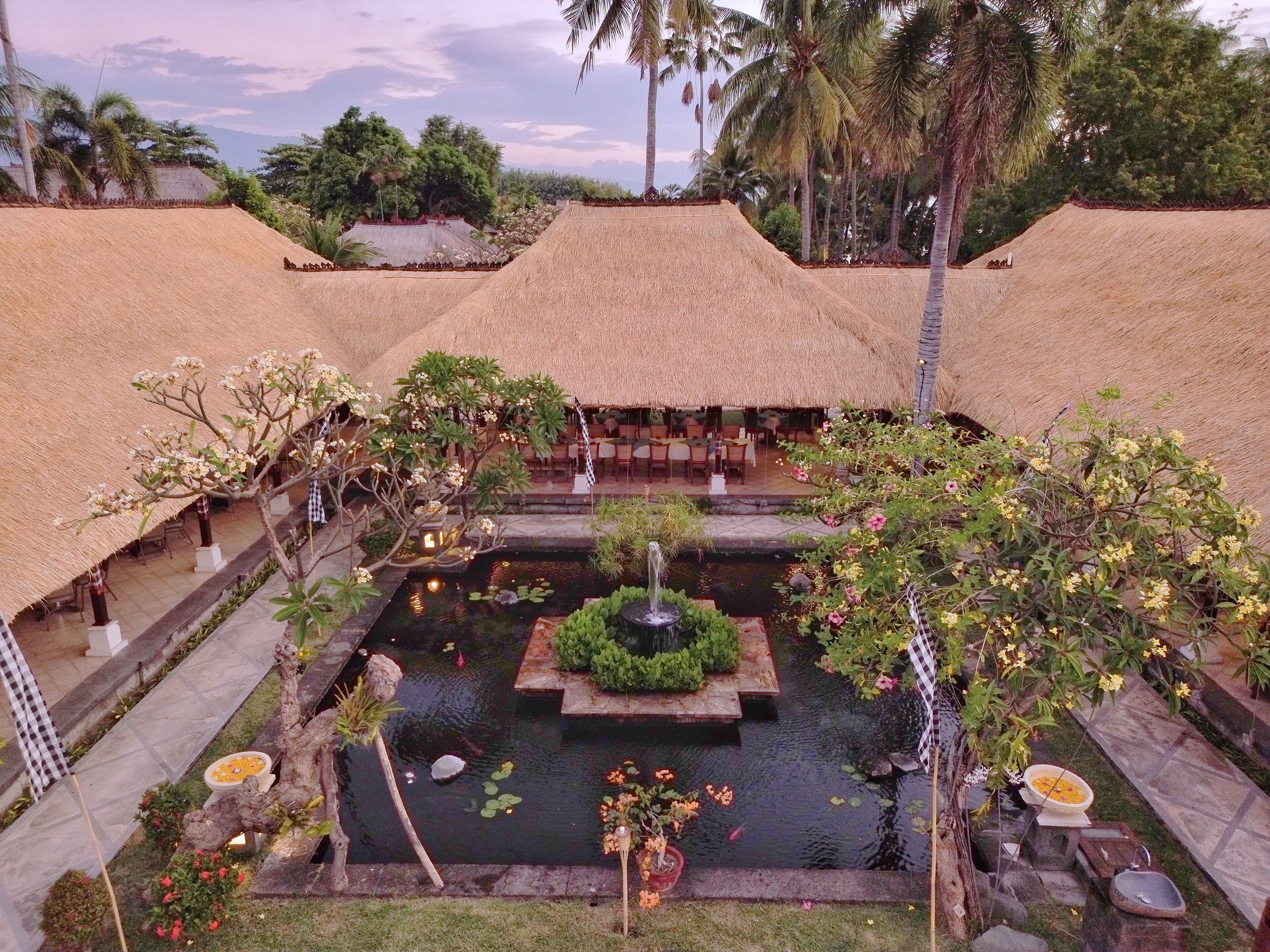 Un resort con cabañas de techo de paja, una fuente central y exuberante vegetación tropical.