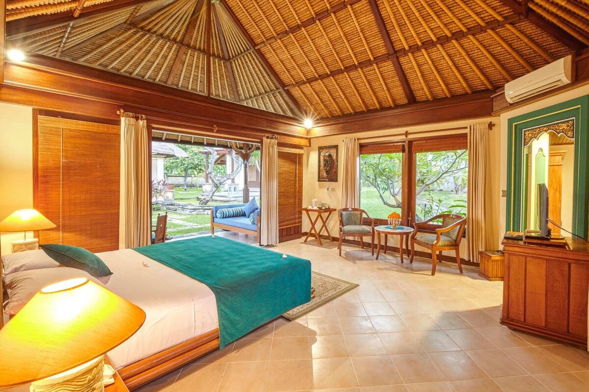 A spacious bedroom with a large bed, a sitting area with chairs, a small table, and a view of the outdoors.