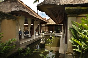 A traditional thatched-roof building with a water feature in the foreground. - Puri Bagus Lovina (Buleleng)