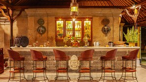 A bar area with a stone counter, four wicker bar stools, and a decorative Buddha statue. - Puri Bagus Lovina (Buleleng)