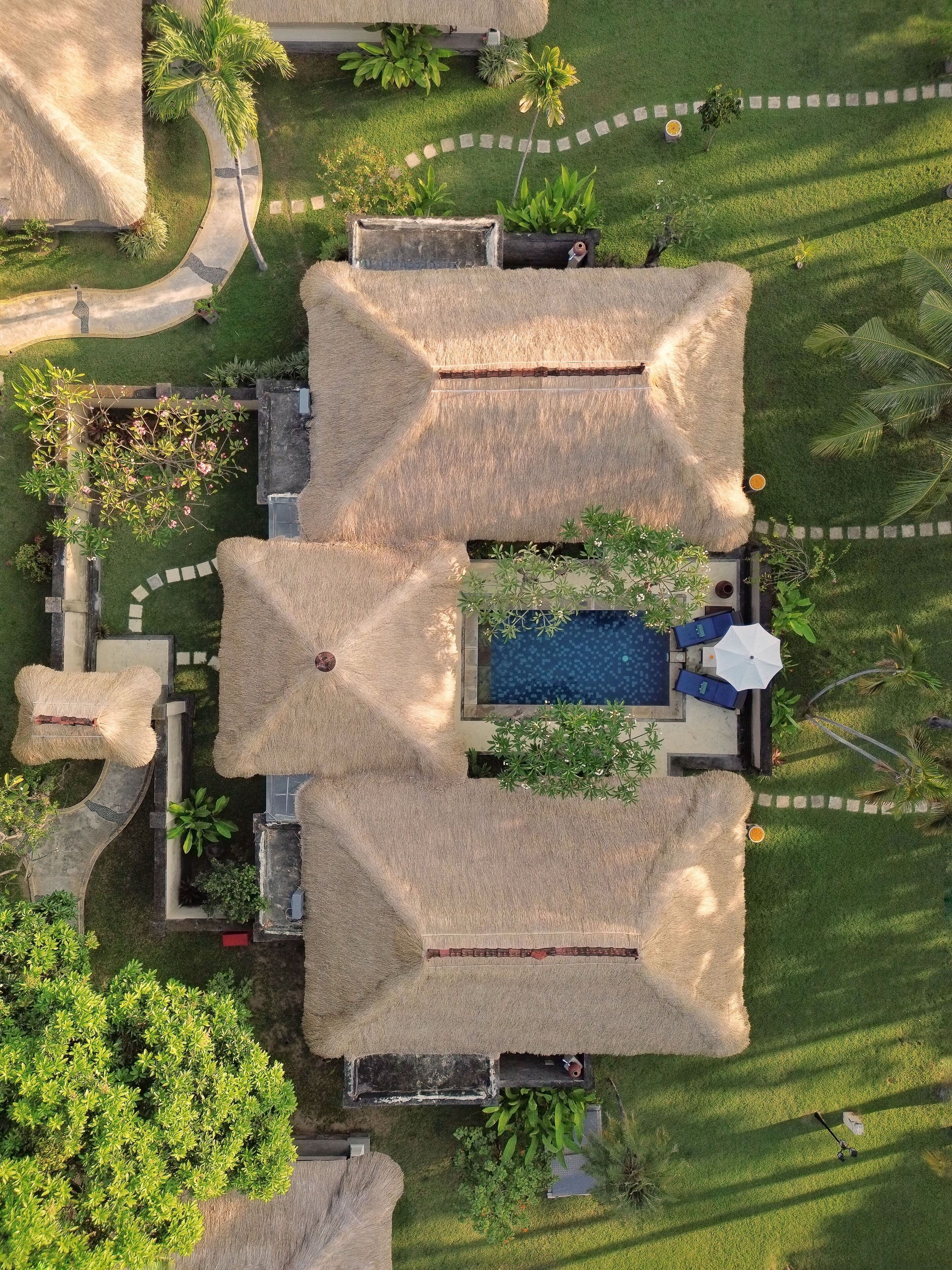 Vista aérea de un complejo turístico con estructuras de techo de paja, una piscina y un césped bien cuidado.