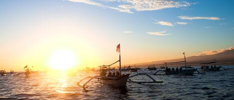 Un coucher de soleil sur une étendue d’eau, avec plusieurs bateaux et un bateau amarré portant un drapeau.