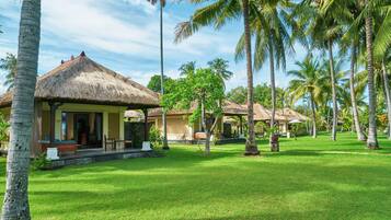 Un resort con cabañas de techo de paja, palmeras y un césped bien cuidado.
