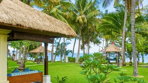 A tropical resort with thatched-roof huts, palm trees, and a bench with cushions. - Puri Bagus Lovina (Buleleng)
