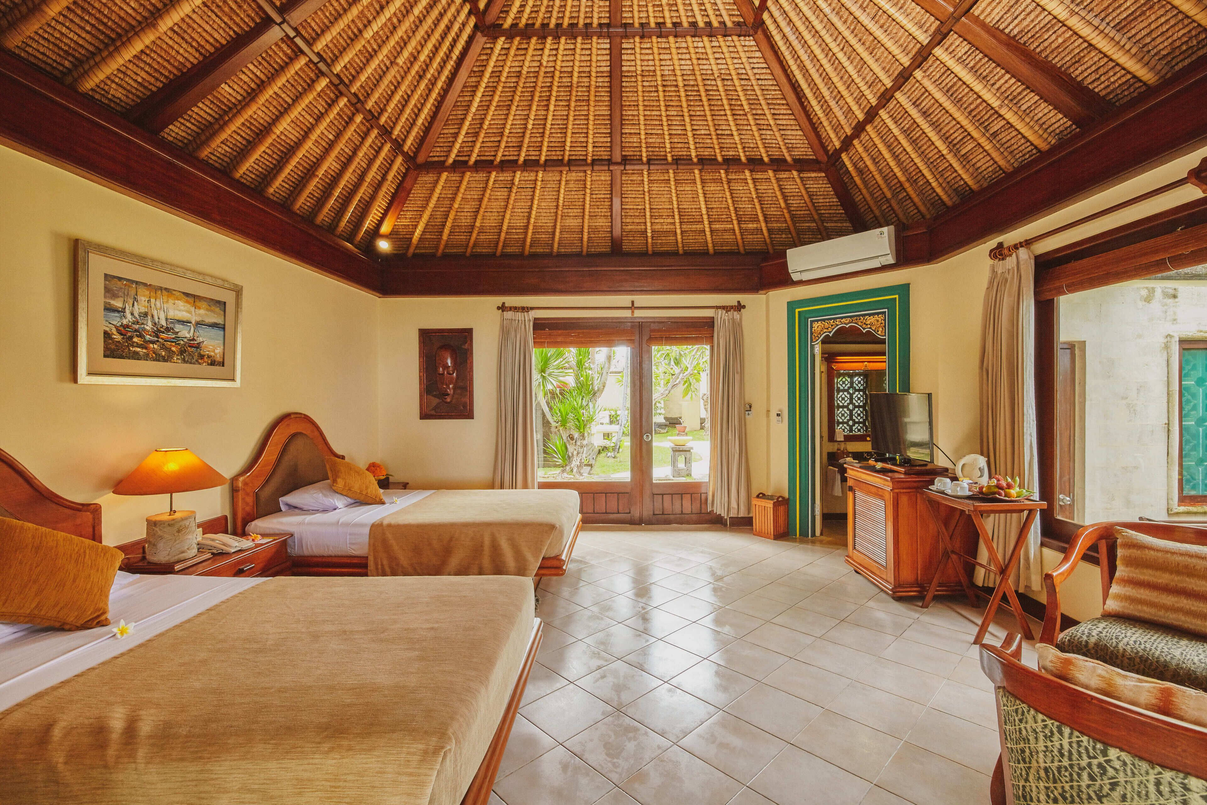 Habitación de hotel con dos camas, techo de madera, escritorio con televisor y vista a zonas verdes.