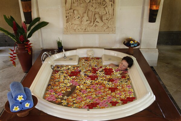 A bathtub filled with flowers, a potted plant, and a towel rack with towels.