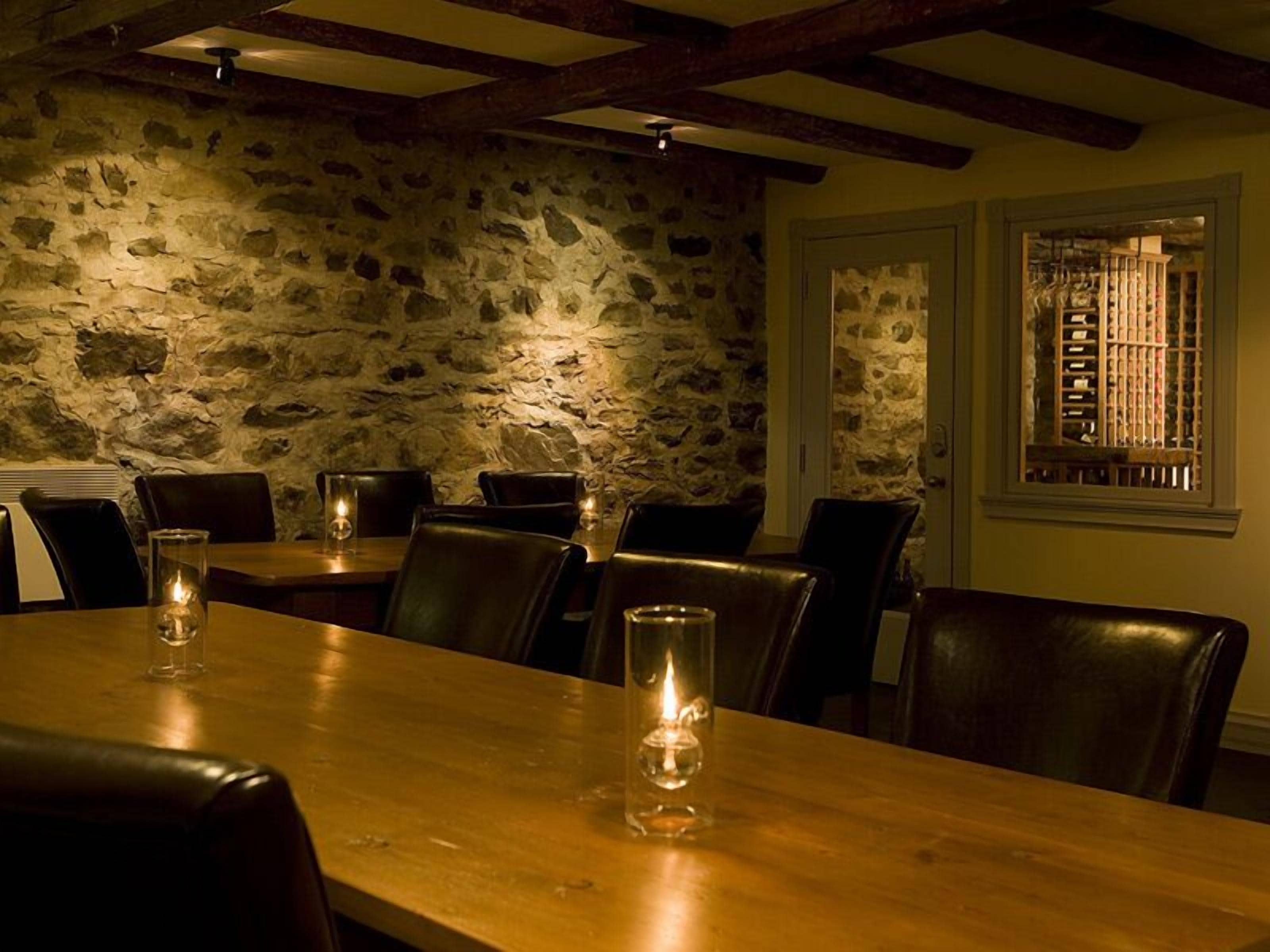 A dining area with stone walls, wooden beams, and leather chairs.