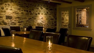 A dining area with stone walls, wooden beams, and leather chairs.