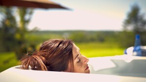 A person reclining in a bathtub with a blurred outdoor background. - Auberge West Brome (Lac-Brome)