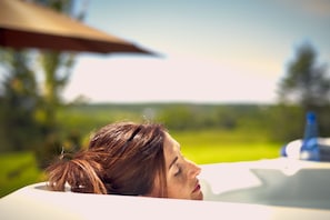 A person reclining in a bathtub with a blurred outdoor background. - Auberge West Brome (Lac-Brome)