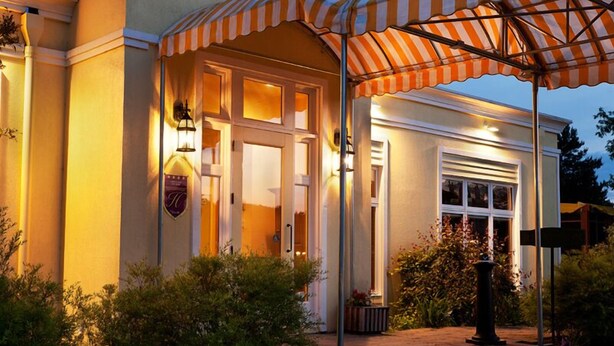L’entrée d’un hôtel, avec un patio abrité, une façade bien éclairée et un jardin aménagé.